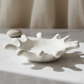 A white ceramic dish designed in the shape of a milk splash, shown on a clean white background with a soft shadow underneath.